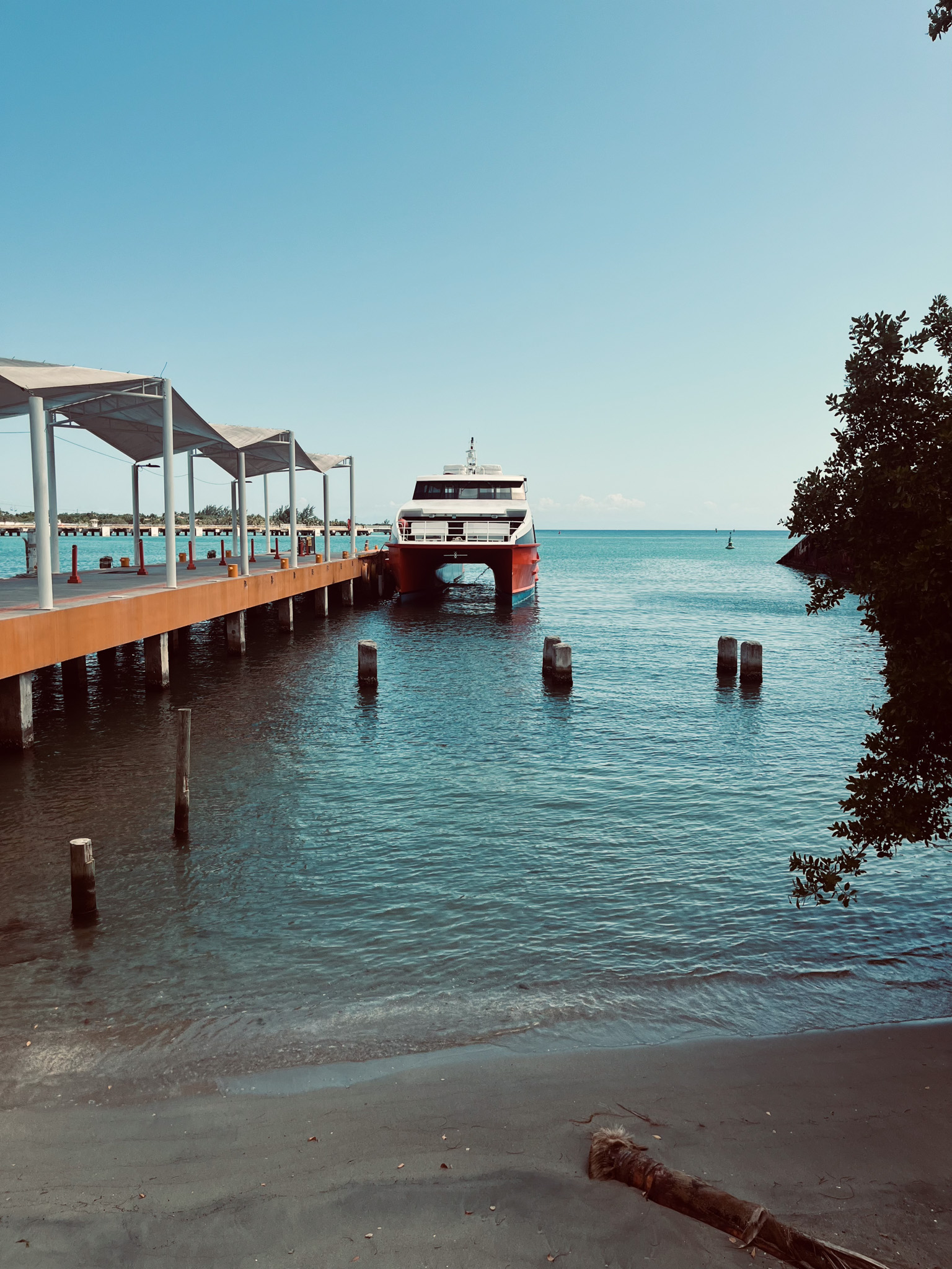 view from the beach of a ferry at deck in Roàtan, Honduras ready to depart for Utila. On the left side of the image, passenger pontoon leads to the boat. the sea is calm, on a clear and sunny day