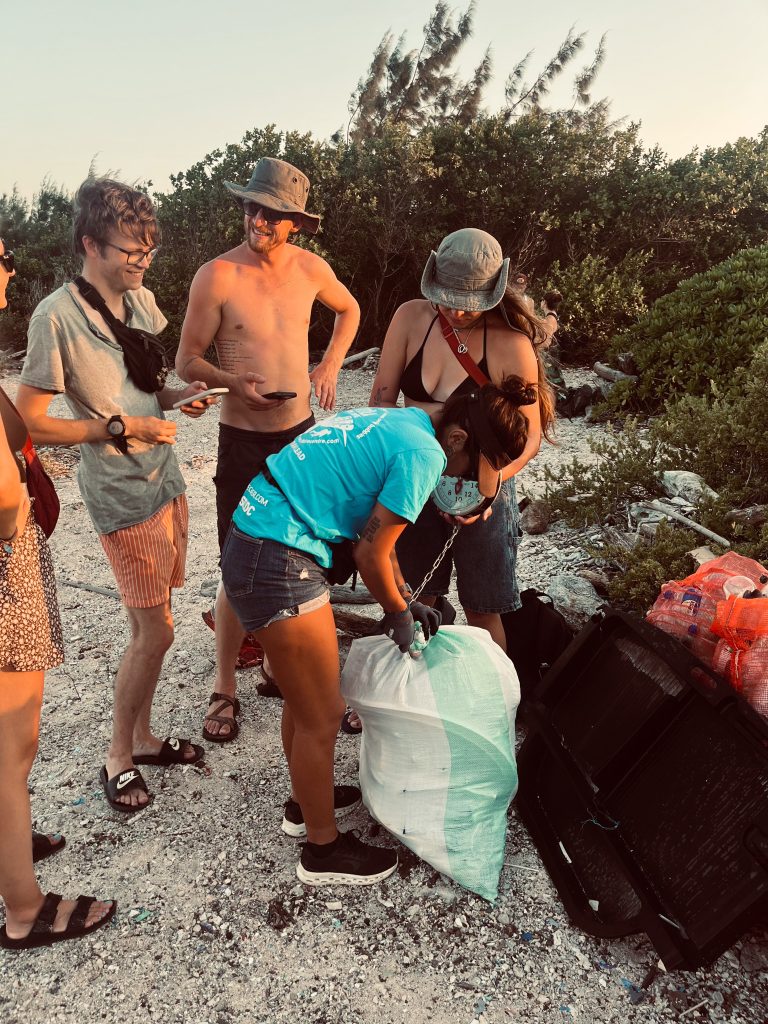 view of several people on a beach, weight bags of trash after a beach clean