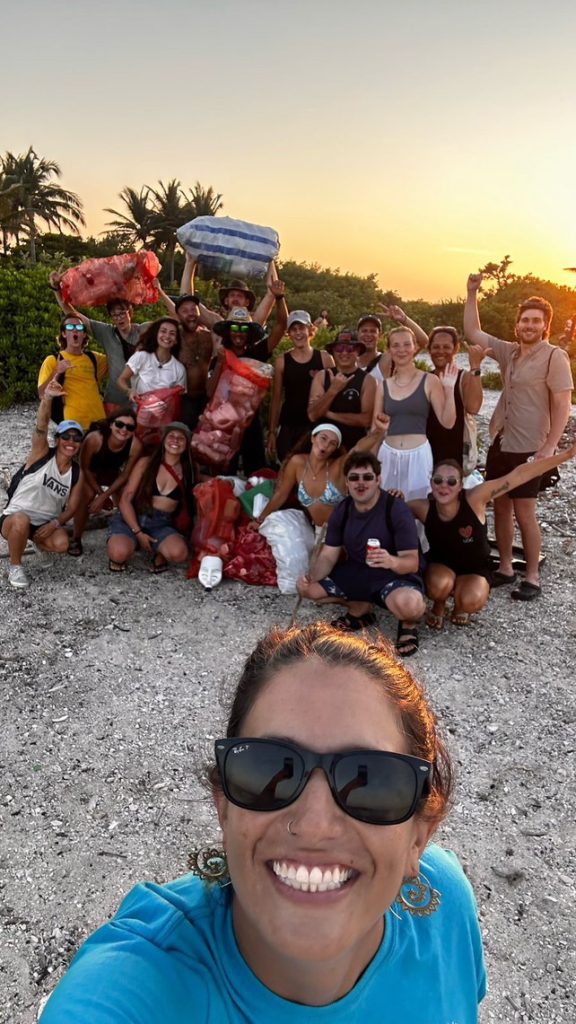 Group photo by sunset after a successfull beach clean; photo taken as a selfie by person in a blue shirt on the forefront