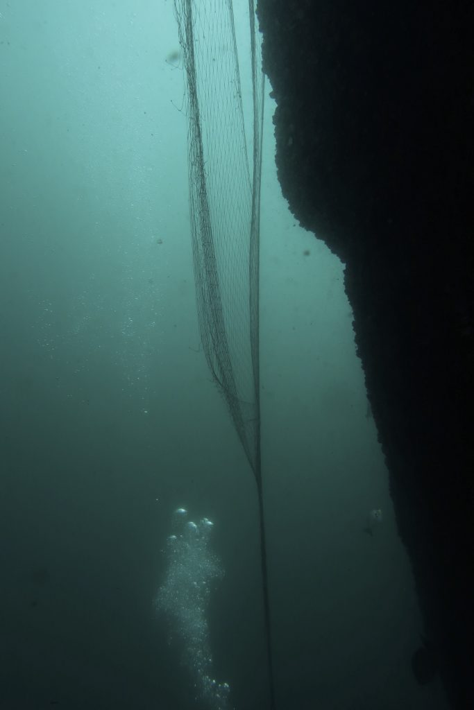 underwater view of a ghost fishing net tangled on a boulder and loose in water, representing a hazard for marine life and divers.